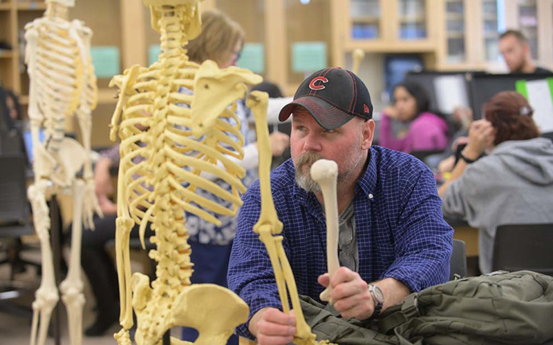 A male student at a lab table is examining the human anatomy skeleton model.