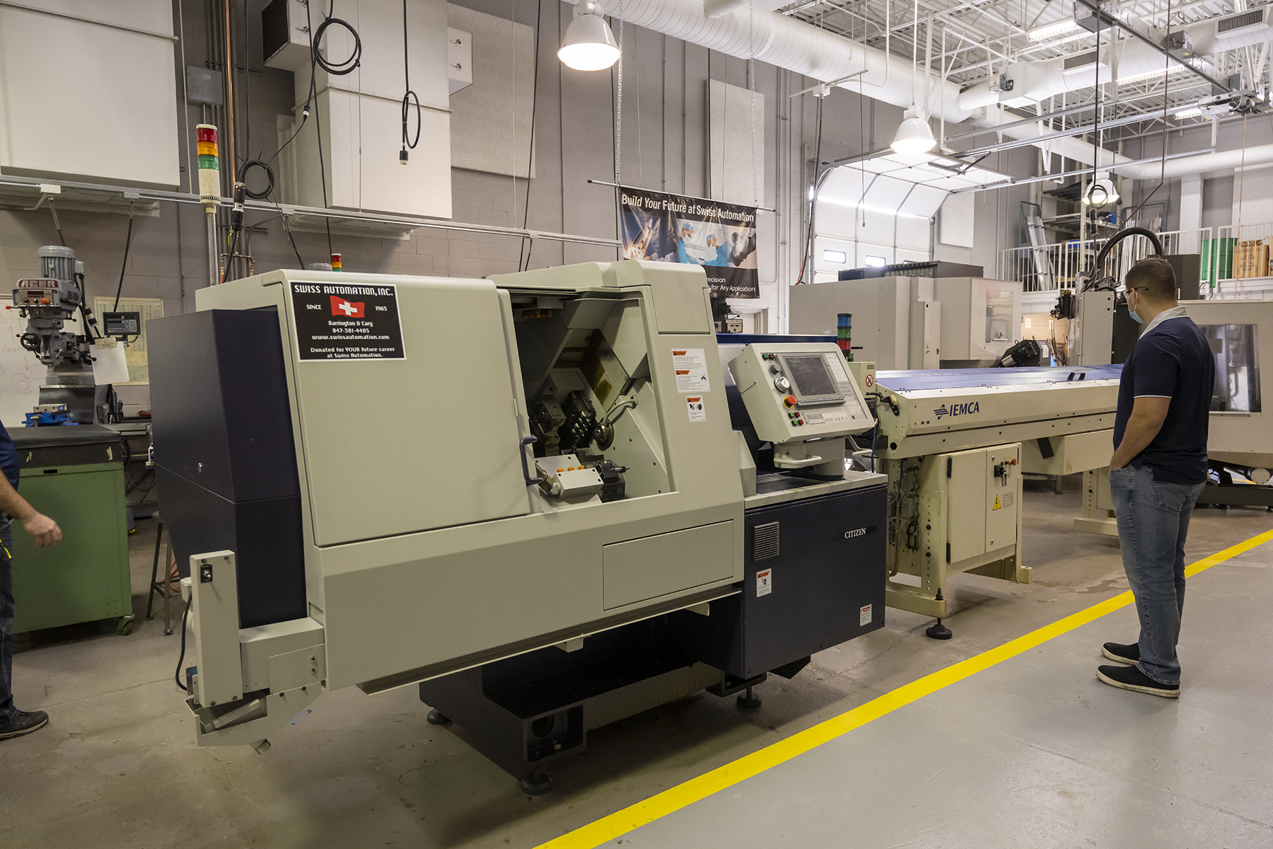 Alejandro Murillo, instructor of IMT/CIM, admires the 9-axis machine donated by Swiss Automation, Inc