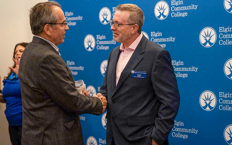Two gentlemen shaking hands in front of a backdrop