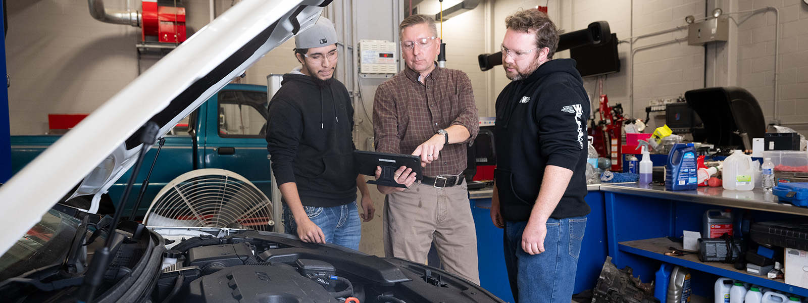 two students working with instructor next to car