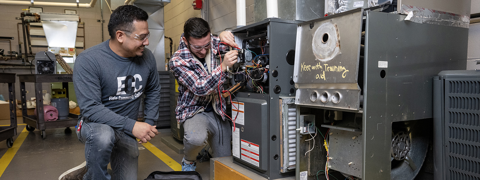 A student working on an HVAC unit as instructor supervises.