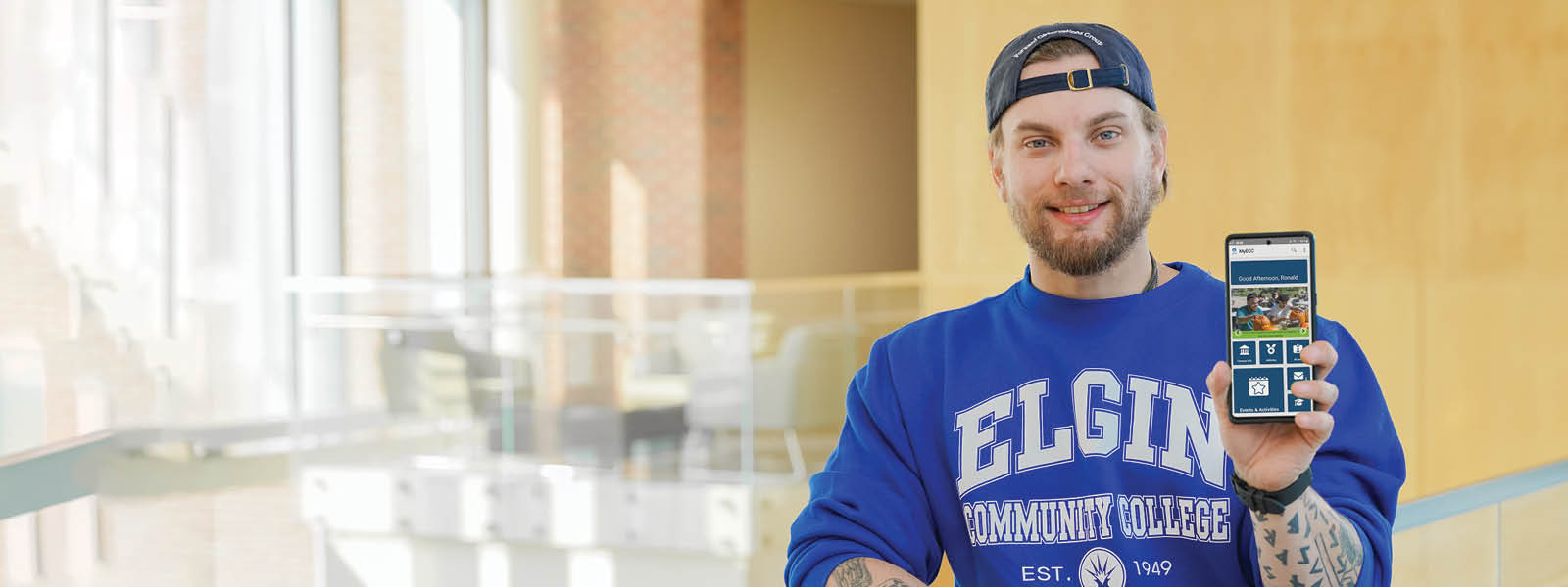Male student with Elgin Community College apparel holding smart phone, with myECC Experience app open.