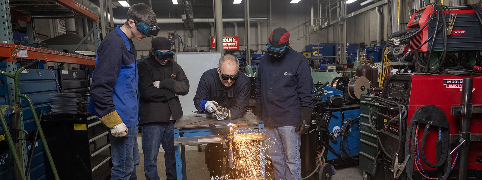 Students observe a professor welding material.